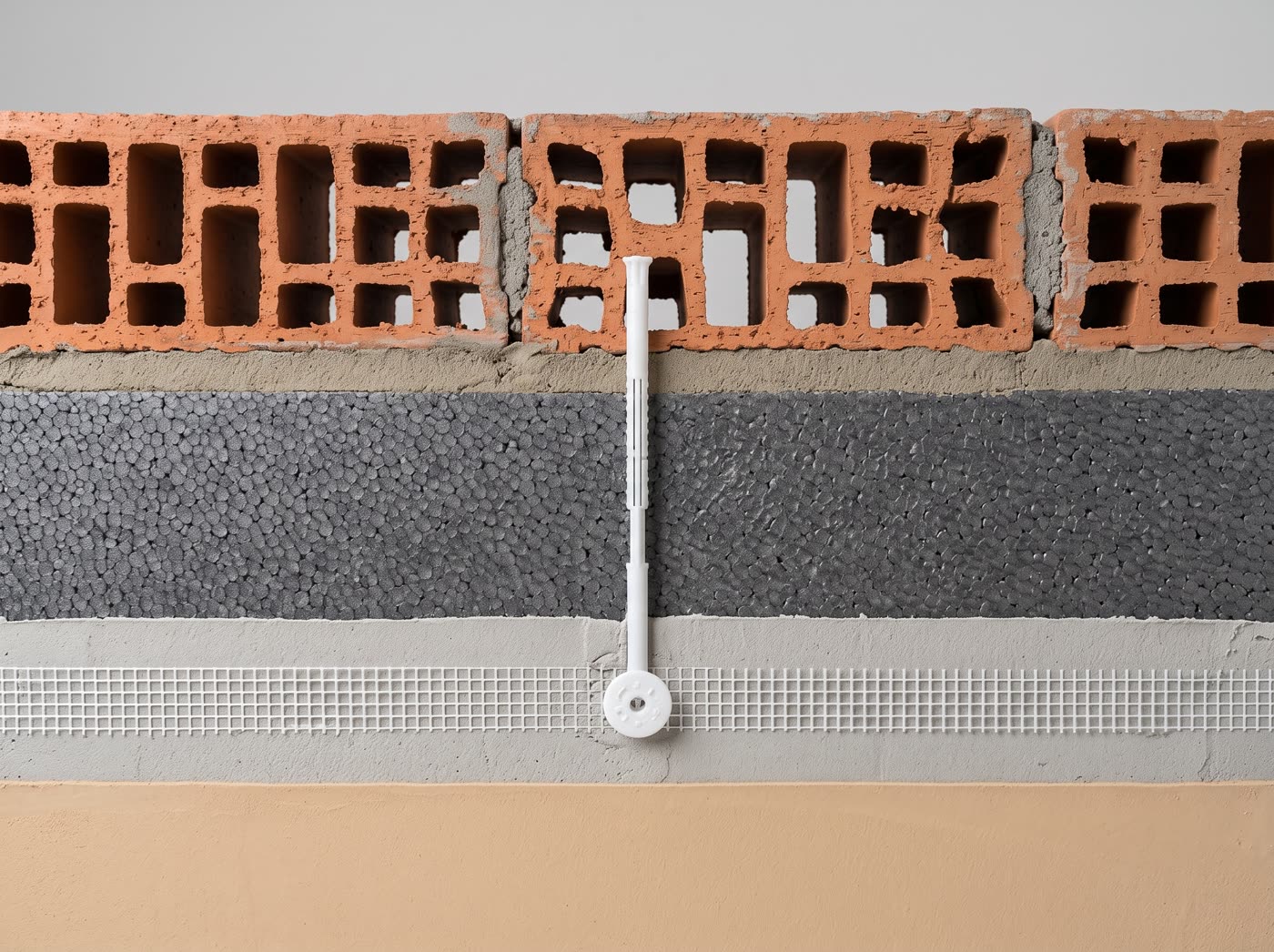 Sezione del muro con cappotto termico: muratura, collante, pannello isolante, rasatura armata, intonaco di finitura